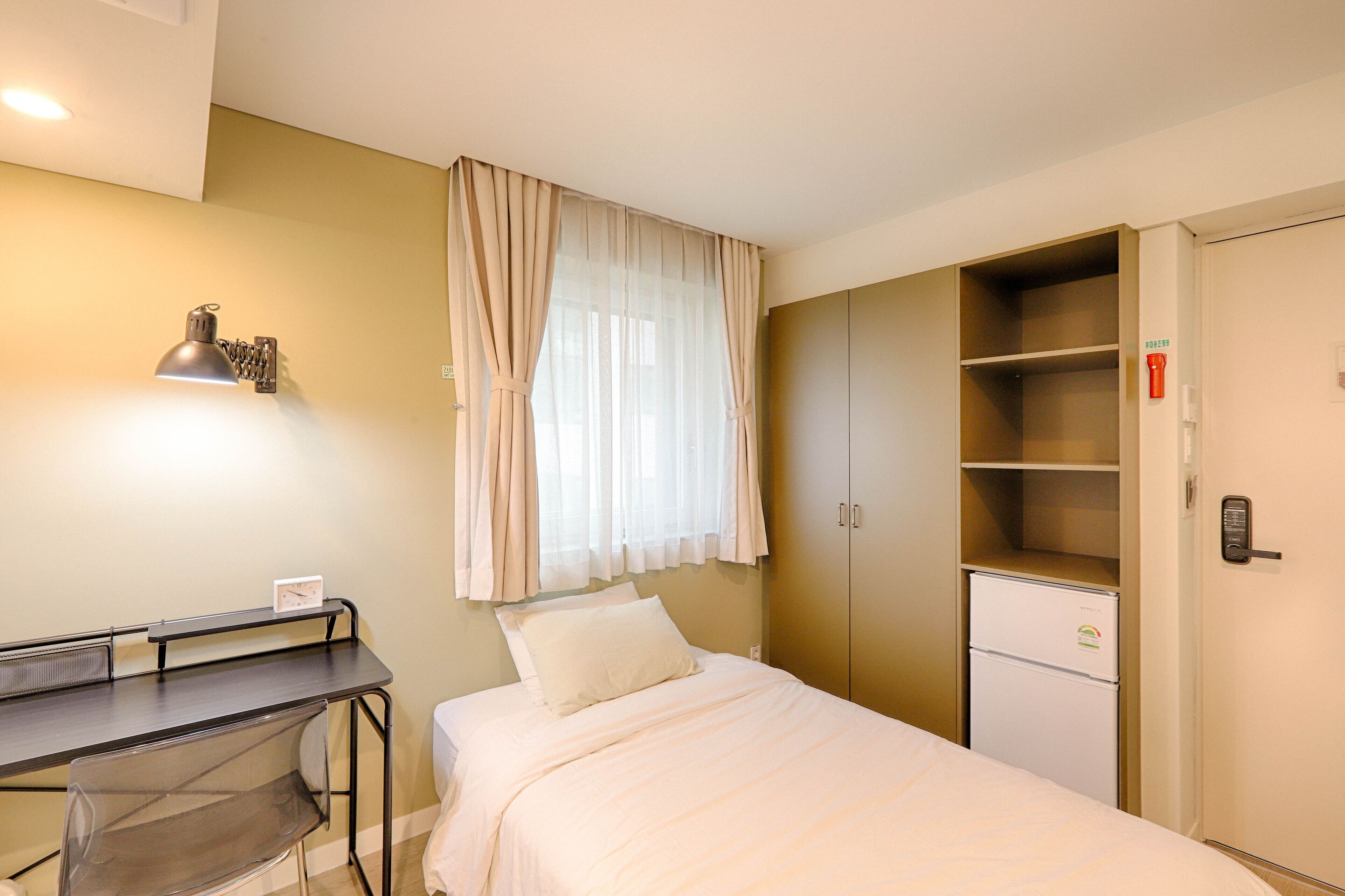 Habitación de hotel con cama, escritorio, silla, armario y un refrigerador pequeño.