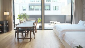 Ein Hotelzimmer mit einem großen Bett, einem Esstisch mit Stühlen, einem kleinen Balkon mit Tisch und Stühlen sowie Blick auf die Stadtgebäude.
