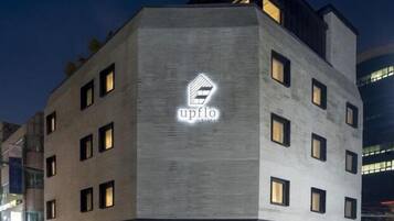 A modern hotel building with a prominent logo on the facade, multiple windows, and a well-lit entrance.