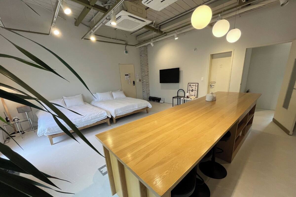 Moderni hotellihuone, jossa on puinen ruokapöytä, kaksi erillistä sänkyä, televisio ja yksi seinä, joka on koristeltu tiilillä.