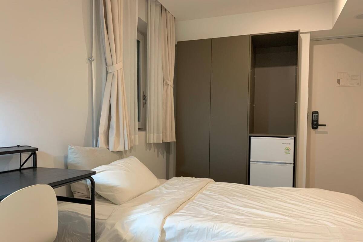 Hotellihuone, jossa on sänky, työpöytä, tuoli, vaatekaappi ja minijääkaappi.