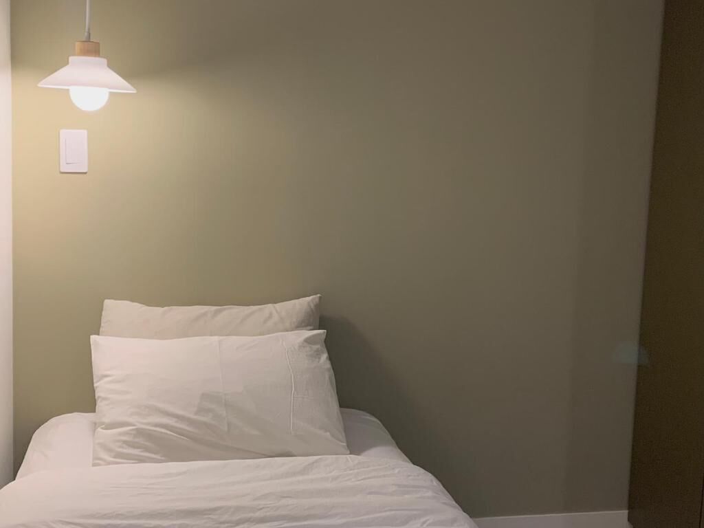A bed with white bedding and pillows, a wall-mounted light fixture, and a light switch.