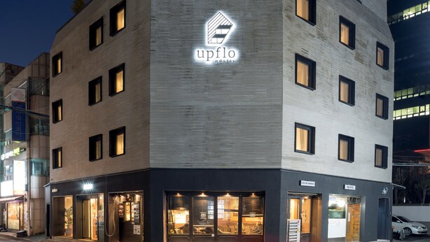 Ein modernes Hotel mit einem gut sichtbaren 'upflo'-Schild, zahlreichen Fenstern und einem Café namens 'Cafe del Sandwich'.