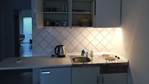 A compact kitchen with a tiled backsplash, a kettle, a sink, and a stove. - Friendly People's Guest House (Zadar)
