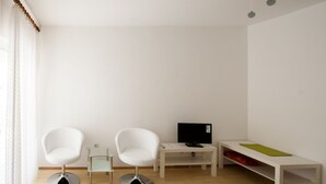 A modern room with two white chairs, a small table with a TV, and a bench with a green mat. - Friendly People's Guest House (Zadar)