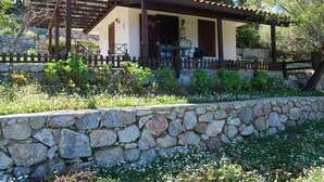 Un bâtiment aux murs de pierre, agrémenté d’une pergola en bois, d’un espace de repos extérieur et d’un chemin pavé.