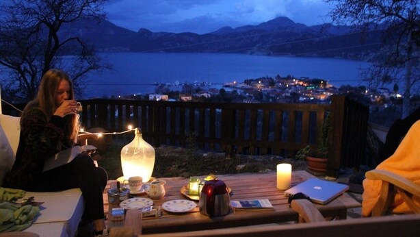 Un espace extérieur aménagé avec des sièges, offrant une vue sur un lac et une ville lointaine, comprenant une table sur laquelle sont disposés divers objets et une bougie.