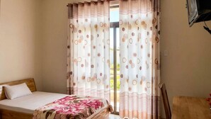 Un dormitorio con una cama, cabecera de madera, ventana con cortinas, aire acondicionado y televisor sobre un mueble.