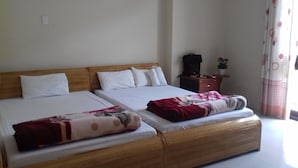 Una cama doble con cabecera de madera, dos almohadas blancas y una colcha roja y blanca. Hay una mesita de noche de madera con una planta y un bolso negro encima.
