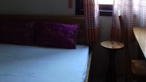 Una habitación con una cama, una mesita y un ventanal con cortinas.