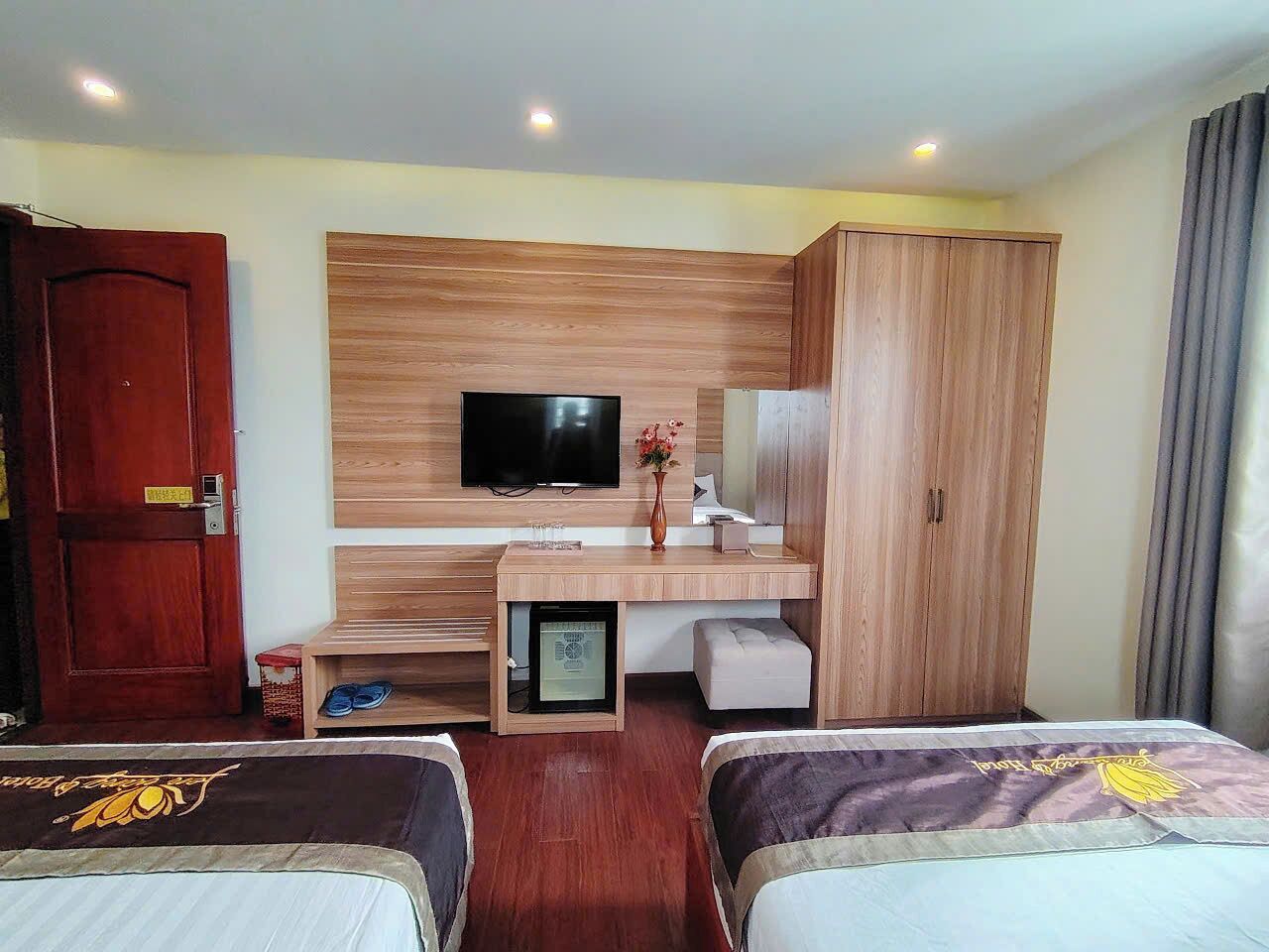 Habitación de hotel con dos camas, televisión, escritorio con computadora, armario y un mueble pequeño.
