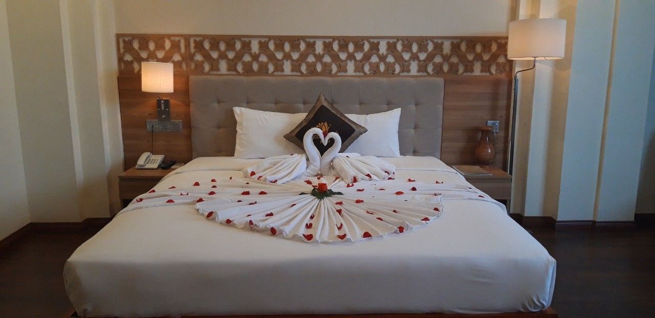 A hotel room with a neatly made bed, a headboard with a patterned design, a bedside table with a lamp, and a nightstand with a phone.