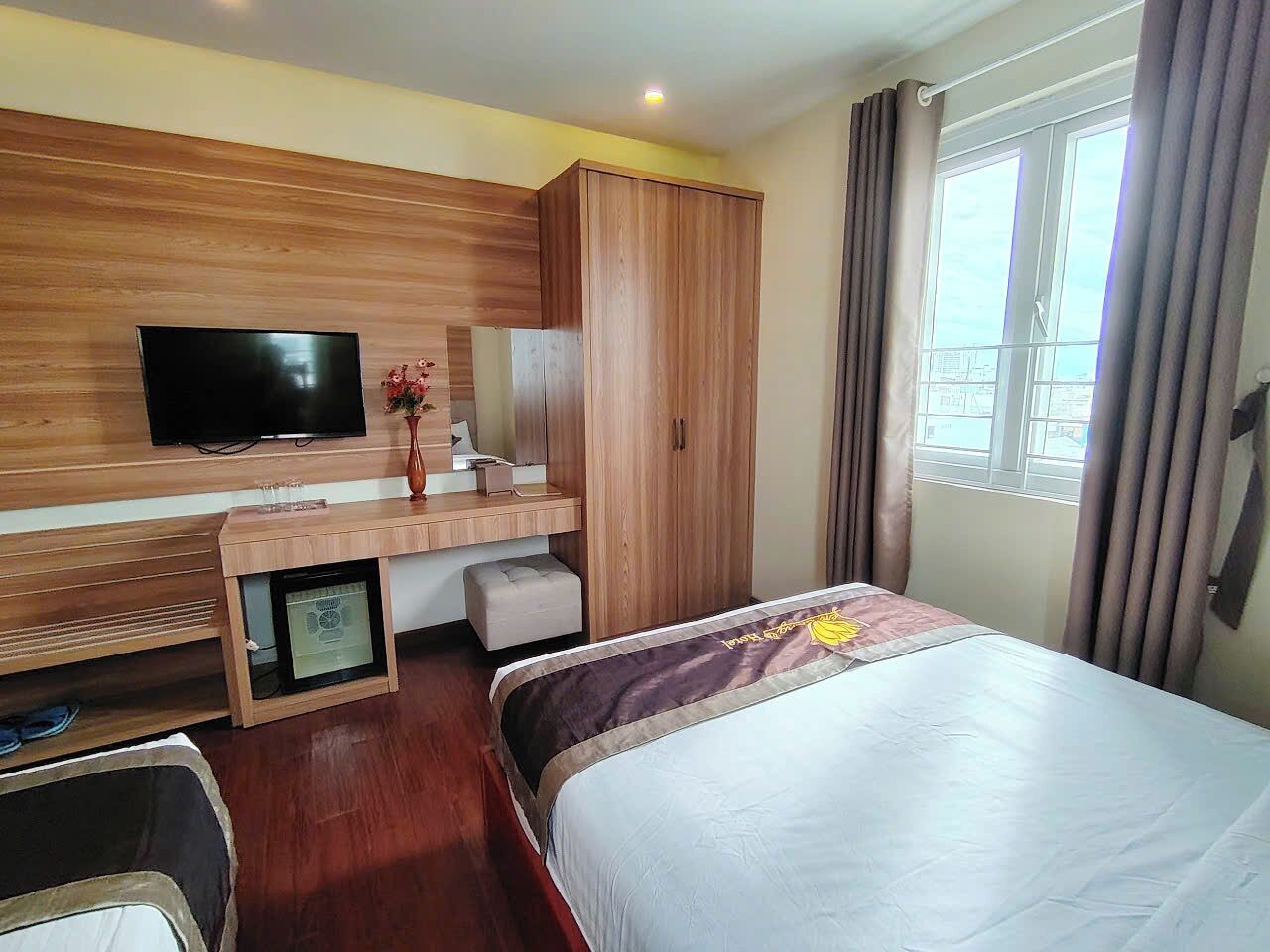 Ein Hotelzimmer mit Bett, Fernseher, Schreibtisch aus Holz und einem Fenster mit Vorhängen.