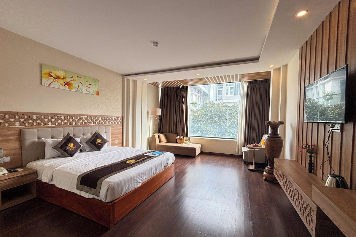 Een hotelkamer met een groot bed, een bank, een televisie en een raam met gordijnen.