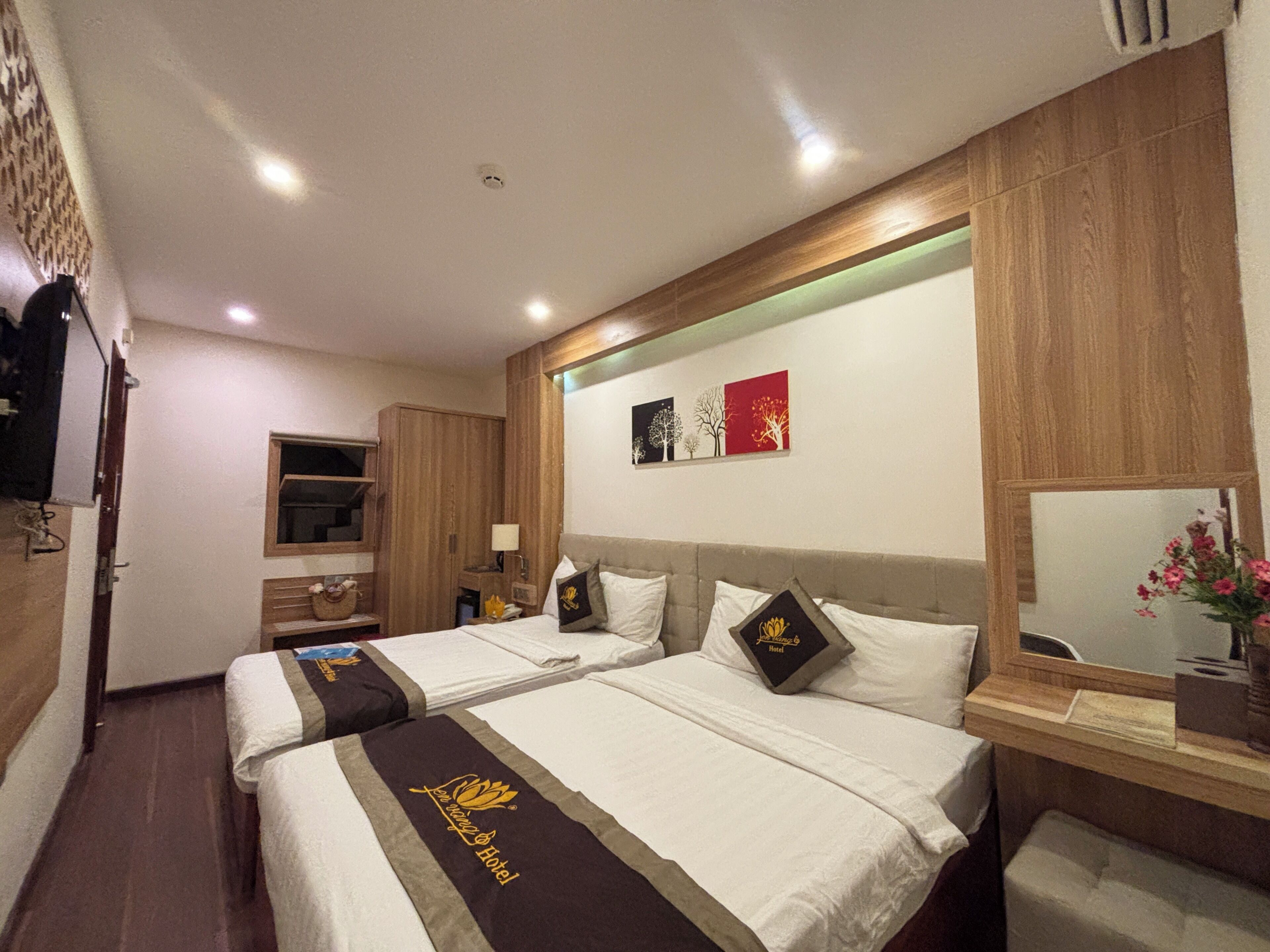 A hotel room with two beds, a wooden headboard, a nightstand, a mirror, and artwork on the wall.