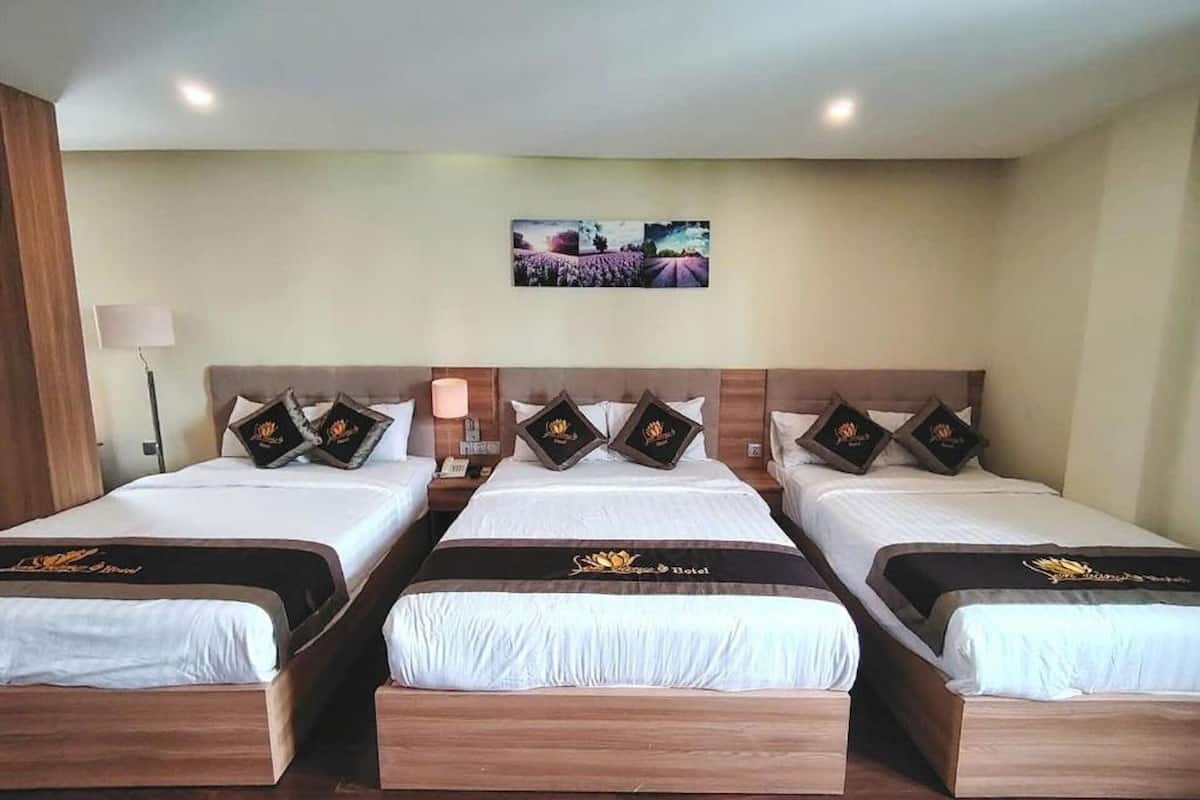 Een hotelkamer met drie eenpersoonsbedden, elk met een houten hoofdbord en een bloemenbeddengoed. Er is een nachtkastje met een lamp en een kleine tafel tussen de bedden. Een ingelijste foto hangt aan de muur boven de bedden.
