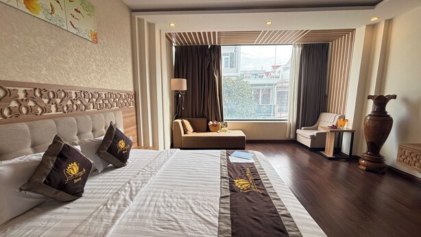 A hotel room with a large bed, a sofa, a small table, and a view of the city through the window.