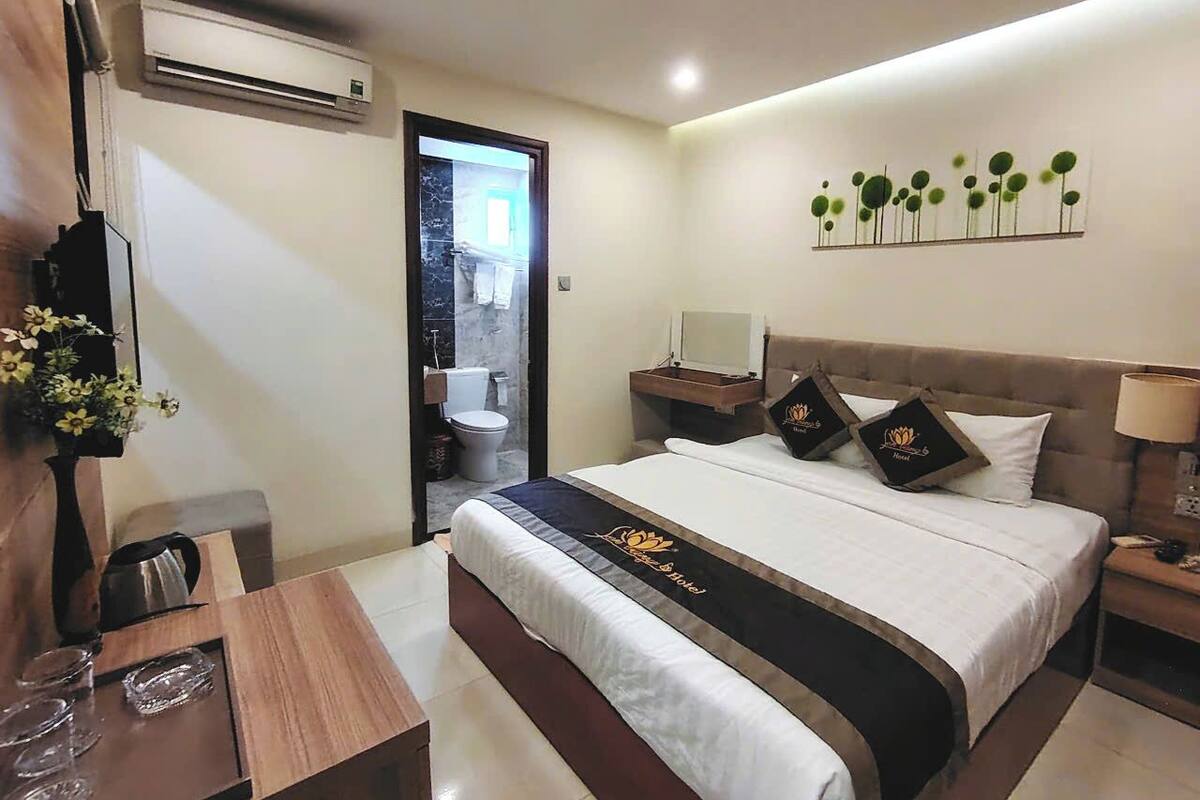 Een hotelkamer met een bed, nachtkastje, lamp en een wandairconditioner.