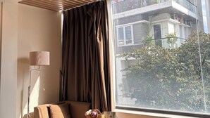 A modern living room with a large window, a sofa, a floor lamp, and a view of a building outside.