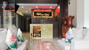 A hotel reception area with a reception desk, two sofas with floral cushions, and a marble coffee table with the hotel name.