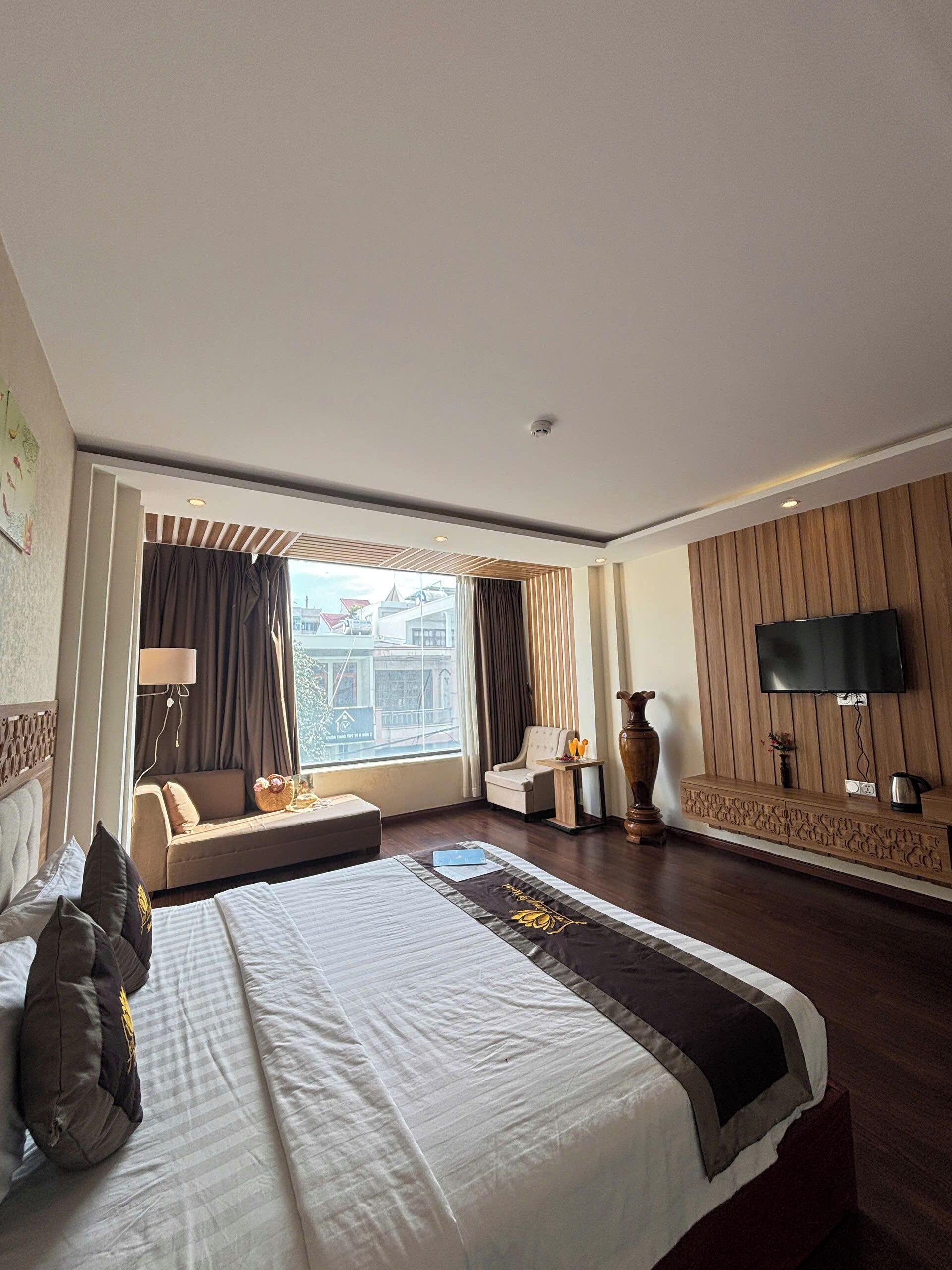 A modern hotel room with a large bed, a TV, a sofa, and a view of the city.