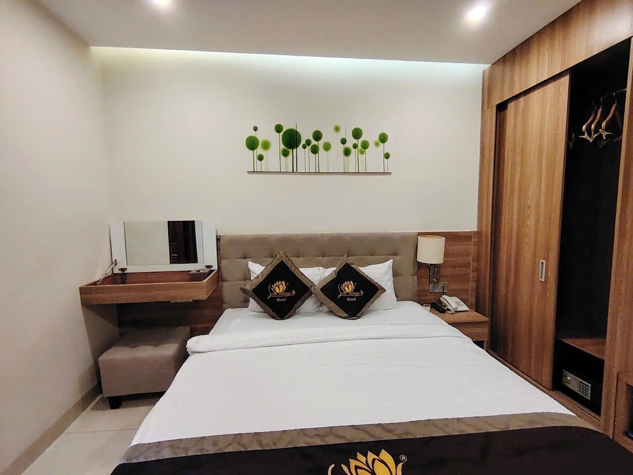 Une chambre d’hôtel comprenant un lit, une table de chevet avec une lampe, un petit bureau avec un miroir et une armoire.