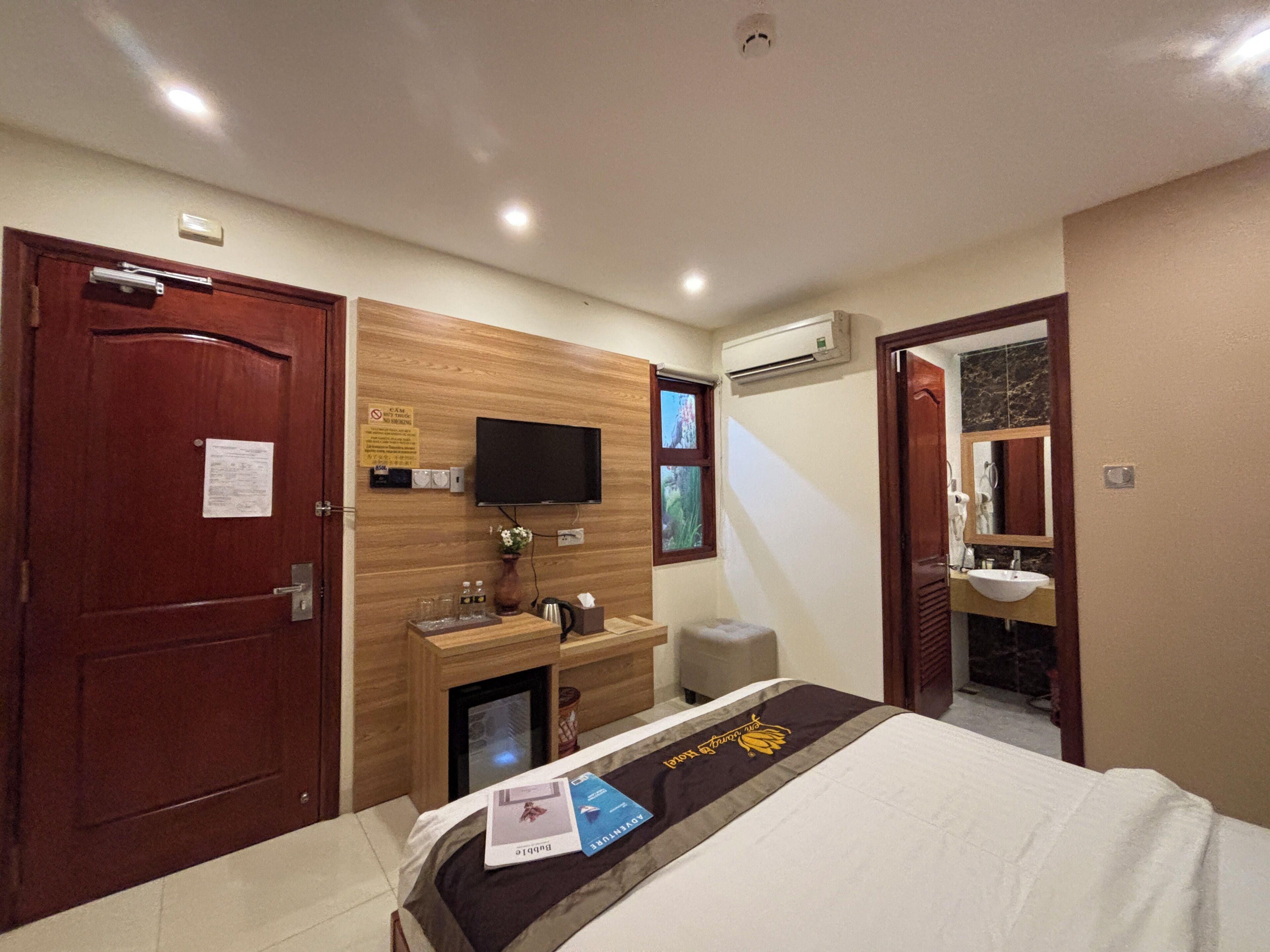 Hotelkamer met een bed, een aan de muur bevestigde televisie, een klein bureau met stoel, een airconditioning en een badkamer met spiegel en wastafel.