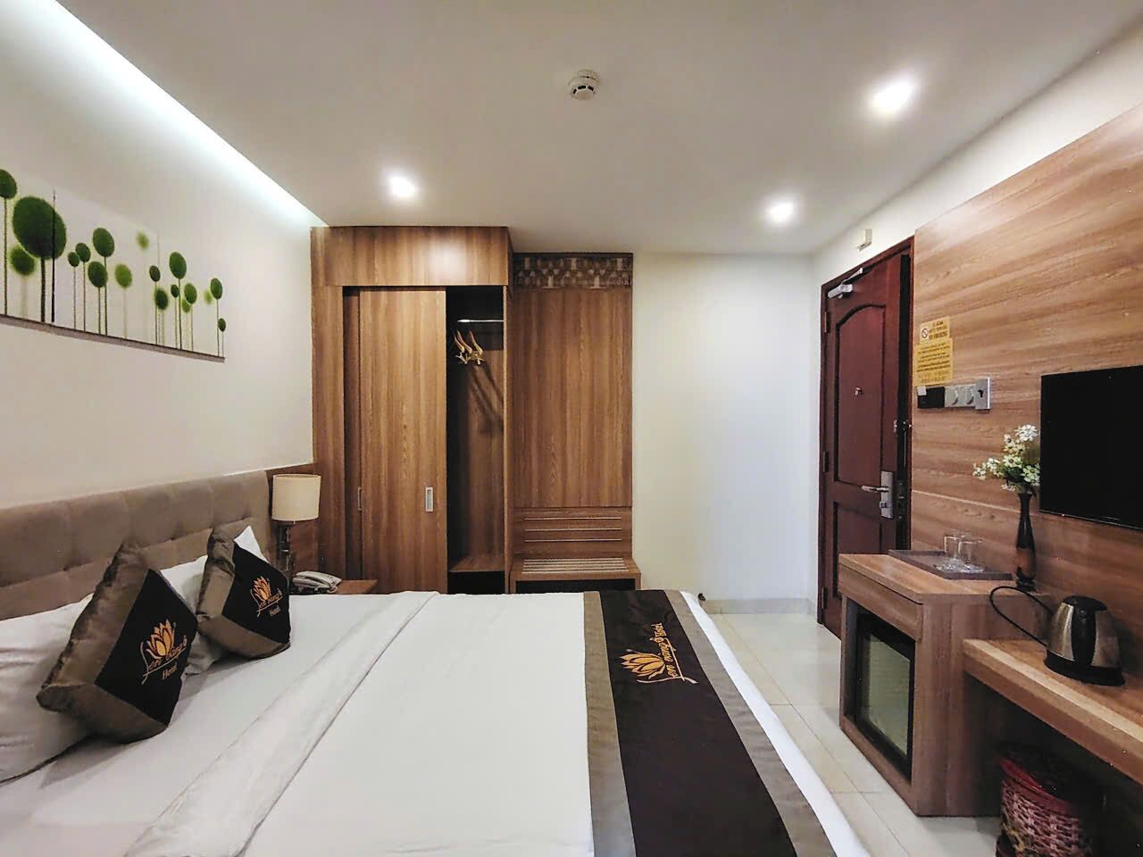 A modern hotel room with a large bed, wooden wardrobe, a small TV, and a kitchenette area.
