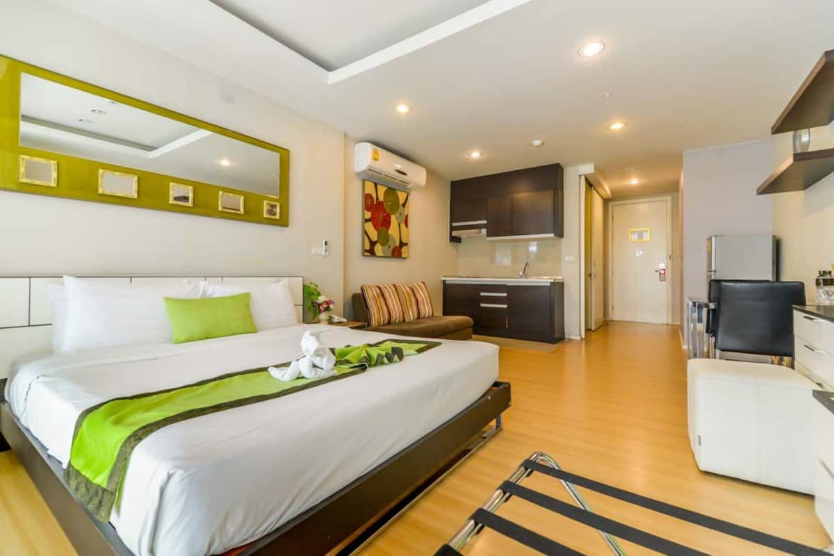 A modern hotel room with a large bed, a small kitchenette, and a separate seating area.