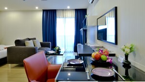 A modern hotel room with a bed, a sofa, a dining table with a vase of flowers, and a flat-screen TV mounted on the wall. - iCheck inn Residence Sukhumvit 1 (Bangkok)