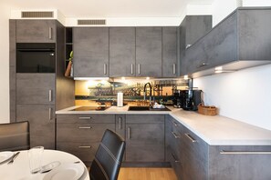 Een moderne keuken met grijze kastjes, een centraal eiland en een eethoek met een stoel en tafel.