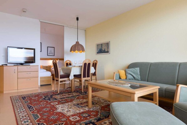 Ein Wohnzimmer mit einer Couch, einem Esstisch mit Stühlen, einem Fernseher und einem gemusterten Teppich.