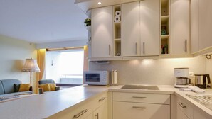 A compact kitchen with a microwave, coffee maker, and a sink. There is a sofa and a lamp in the adjacent living area. - Apartment 178 (ID 092) - House Atlantic (Sankt Peter-Ording)