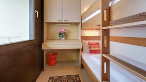 A compact room with a bunk bed, a small wooden cabinet with a shelf, a red basket, and a window with a view. - Apartment 178 (ID 092) - House Atlantic (Sankt Peter-Ording)