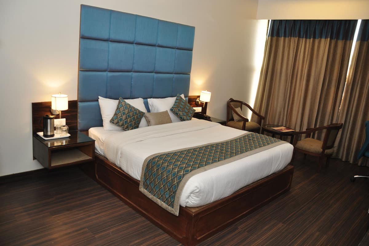 Ein Hotelzimmer mit einem großen Bett, zwei Nachttischen, einem Sessel und einem Fenster mit Vorhängen.