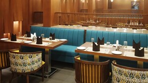 A restaurant with wooden paneling, blue cushioned booths, and tables set with plates, glasses, and napkins. - Hotel Shagun (Dera Bassi)