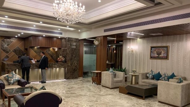 A lobby with marble flooring, a reception desk, sofas, a chandelier, and a clock. - Hotel Shagun (Dera Bassi)