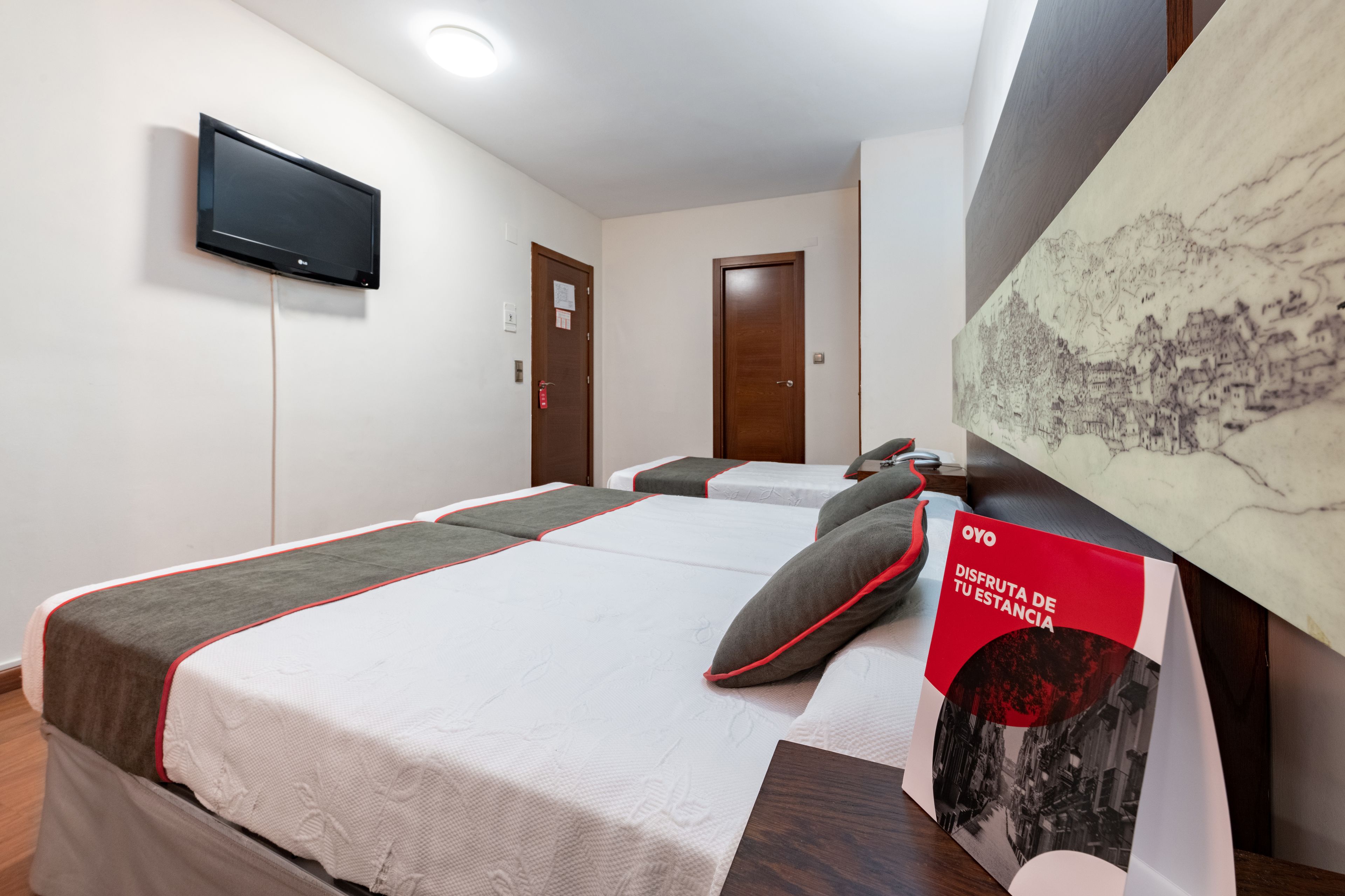 Una habitació d'hotel amb un llit, una televisió penjada a la paret i un quadre a la paret.