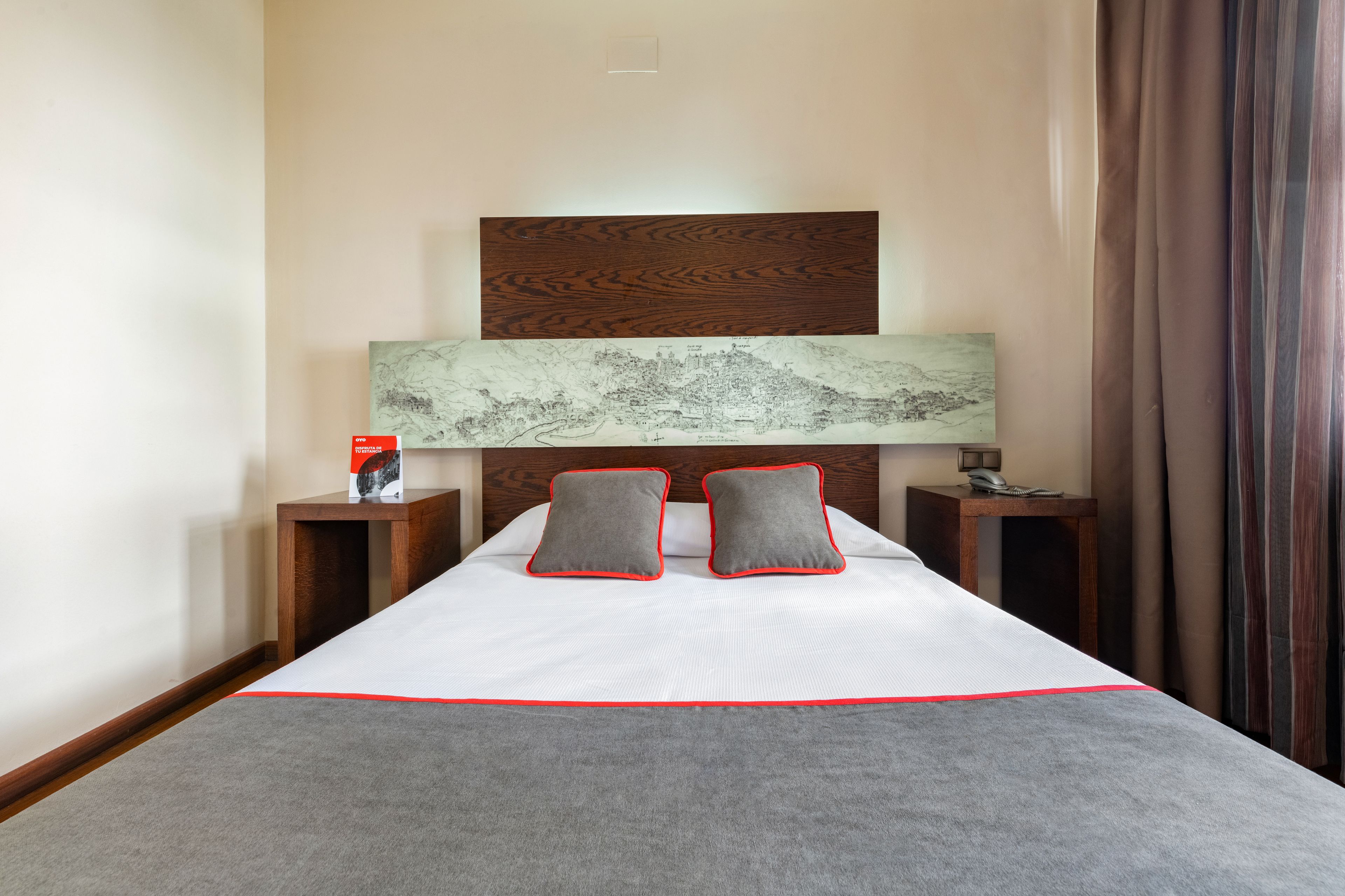 Habitación de hotel con una cama grande, dos mesitas de noche, un cabecero de madera y una obra de arte con un mapa sobre la cama.