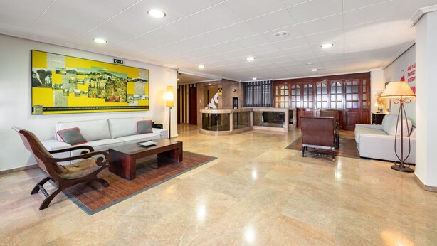 A spacious lobby with a modern design, featuring a large seating area with sofas and a wooden chair, a reception desk, and a large artwork on the wall. - OYO Hotel Francabel (Cuenca)