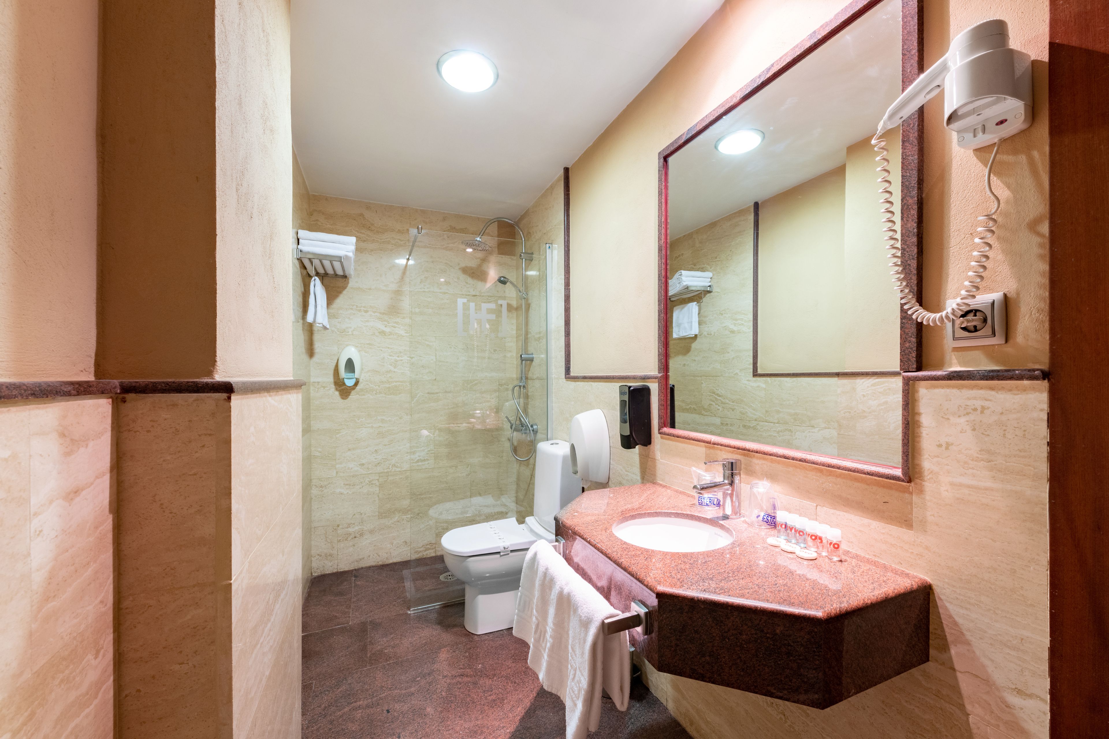 Un baño con piso de mármol, lavamanos con espejo, inodoro y ducha.