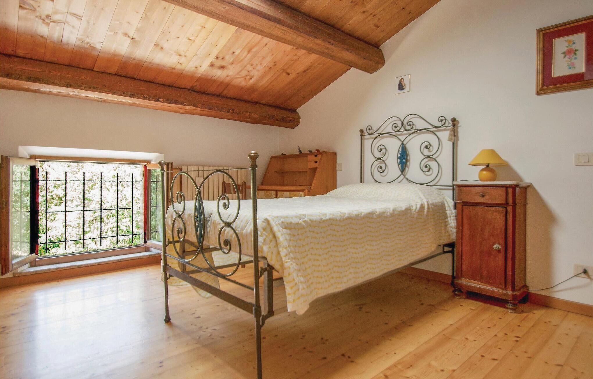 A bedroom with a wooden ceiling, a metal bed frame, a wooden nightstand, and a window with bars.