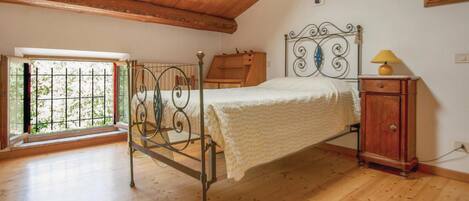 A bedroom with a wooden ceiling, a metal bed frame, a wooden nightstand, and a window with bars.