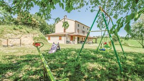 Une maison de campagne avec un patio, une balançoire et un toboggan, le tout installé dans un espace verdoyant.