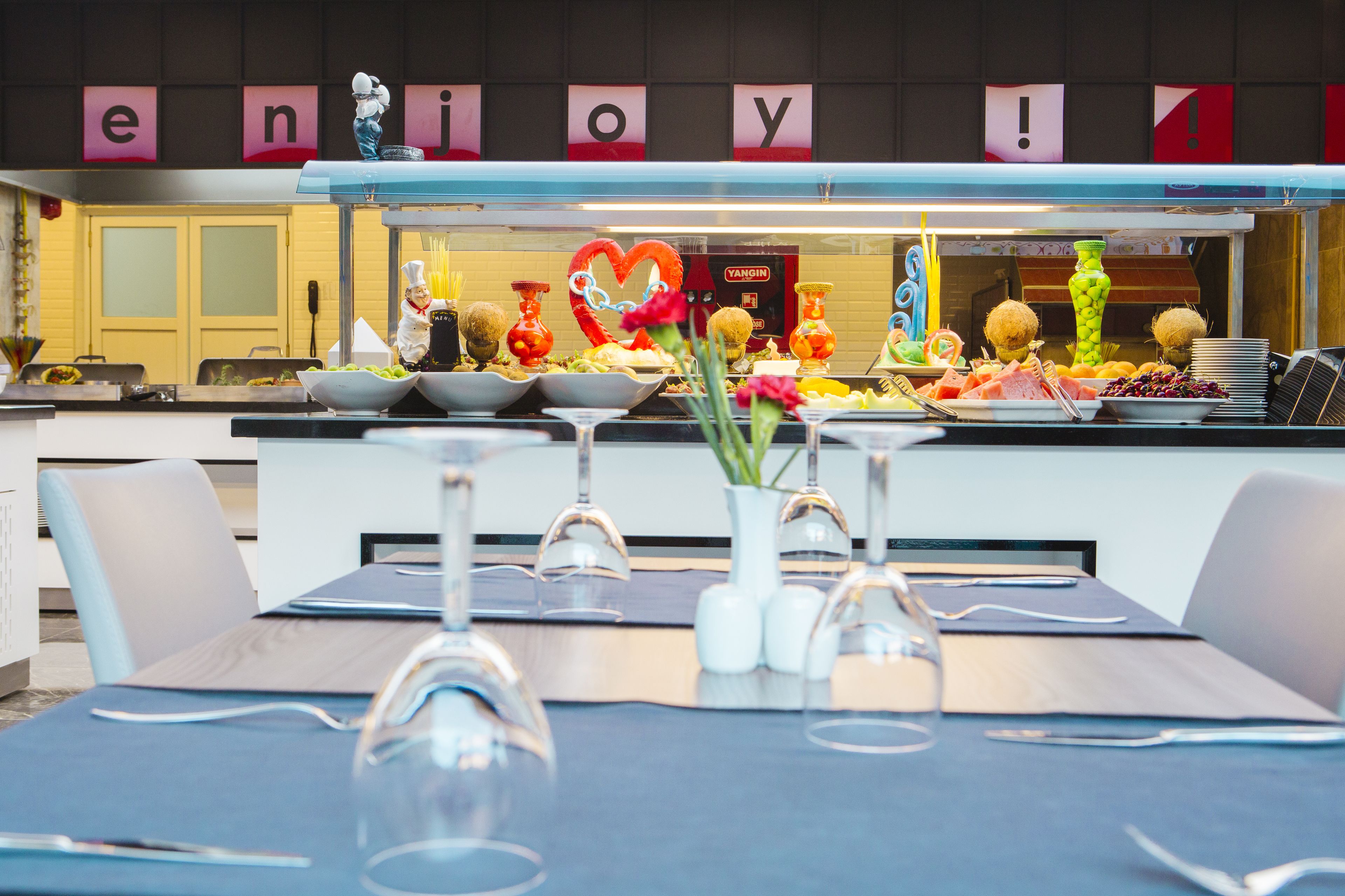 Un restaurant au décor moderne, un buffet proposant une variété de plats, et un panneau sur le mur avec le mot « profitez-en ».