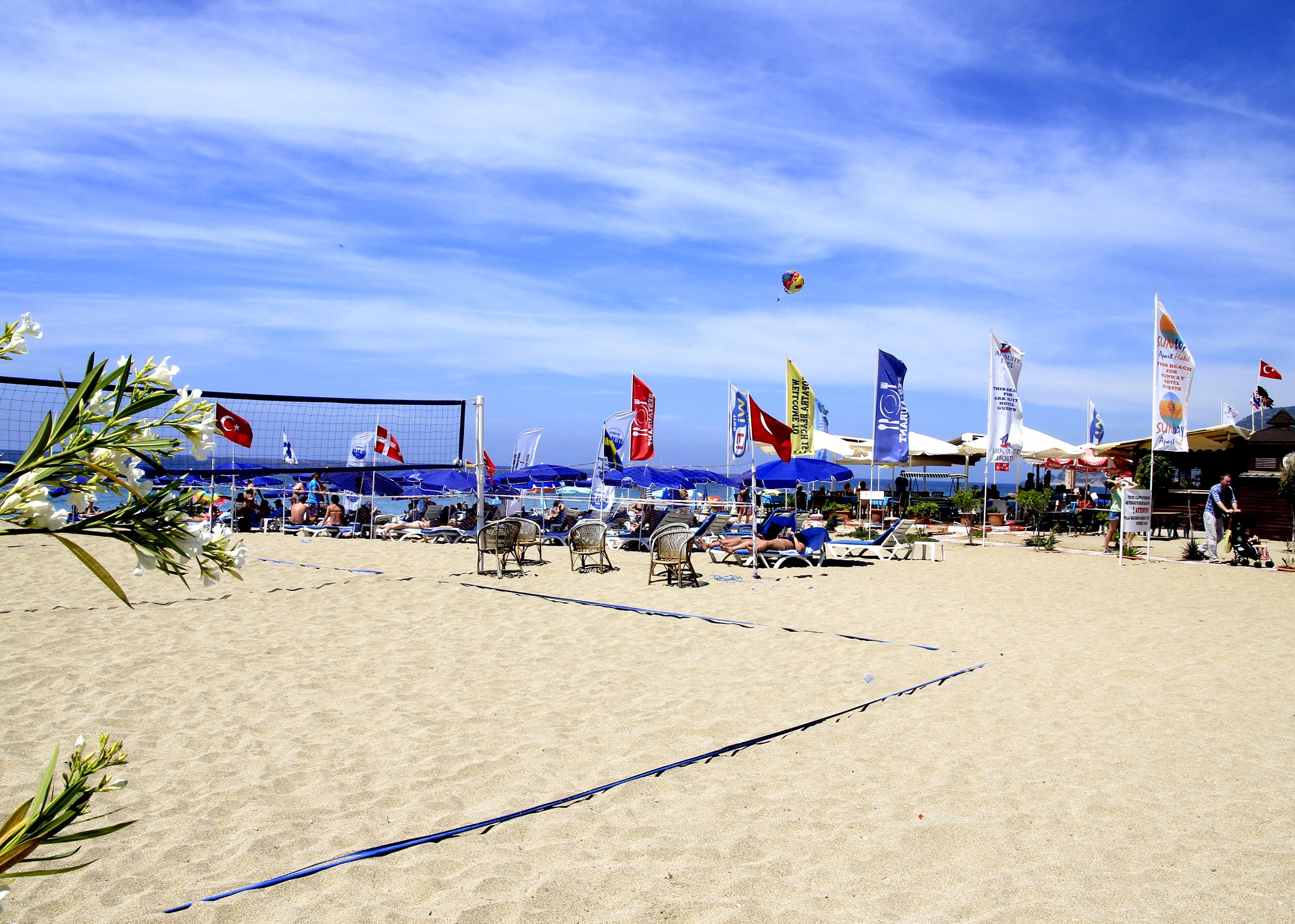 A beach volleyball court with flags, sun umbrellas, and beach chairs.