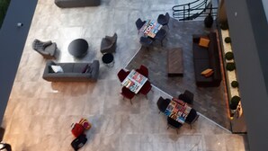 Een ruimte binnenshuis met een hoge plafond, een centraal zitgedeelte met banken en stoelen, en een uitzicht op het buitengebied door grote ramen.