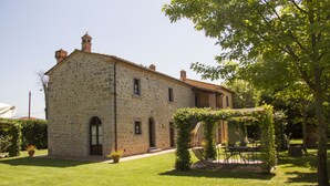 A stone building with a garden, a pergola, and a table with chairs. - Agriturismo il giardino degli ulivi (Cortona)