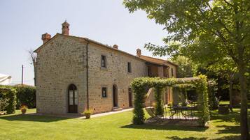 Un edificio in pietra con giardino, una pergola e un tavolo con sedie.
