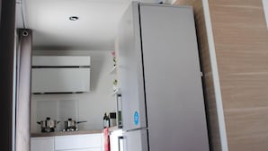 A compact kitchen with white cabinets, a stainless steel refrigerator, and a wooden accent wall. - Agriturismo il giardino degli ulivi (Cortona)
